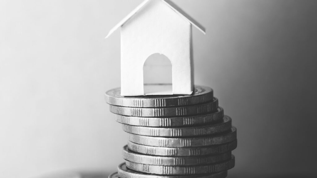 Imagem de moedas empilhadas e ao topo uma casa