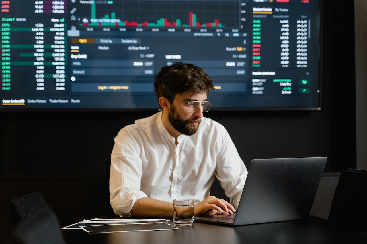 Imagem representando uma corretora de valores, mostrando um investidor operando o mercado em frente uma tela com dados financeiros. 