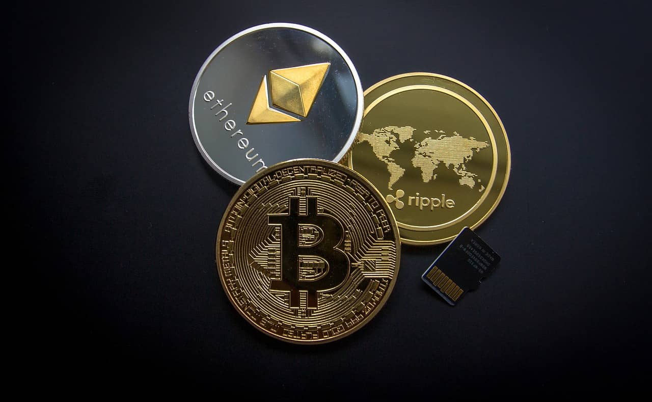 Imagem representando Criptomoedas, mostrando uma moeda de Bitcoin, de Ethereum e de Ripple.