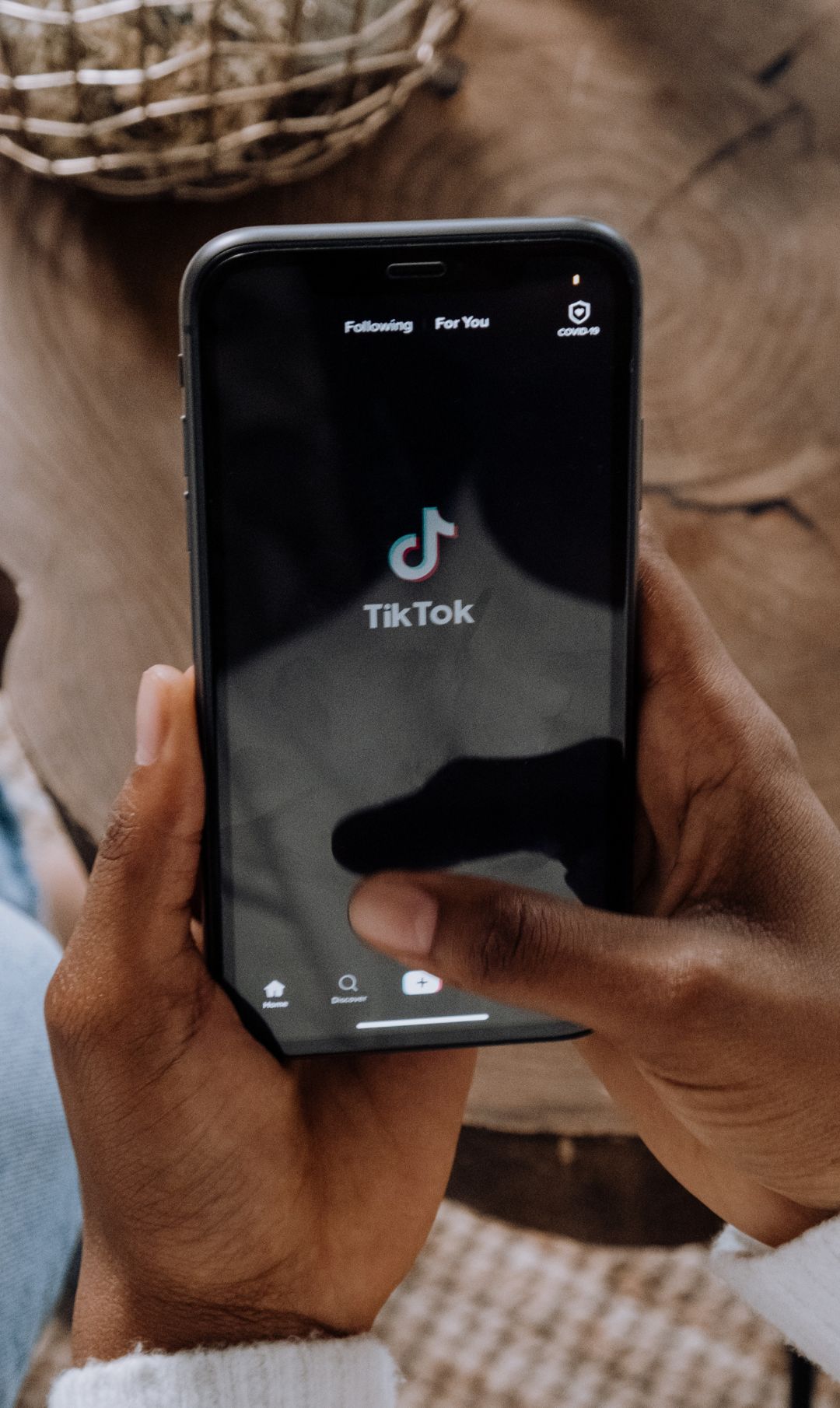 Mãos segurando um celular que está abrindo o app do TikTok