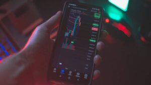 Imagem representando o mercado de capitais, mostrando uma tela de celular com gráficos e indicadores financeiros.